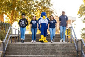 Four students walking down the outdoor steps with Auggie the mascot